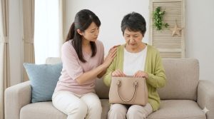 訪問介護で物が盗まれたのではと不安になり、空のカバンを見つめる日本の高齢女性と、寄り添って話を聞く家族（娘）の様子。不安を共有し、冷静な事実確認の第一歩となる。